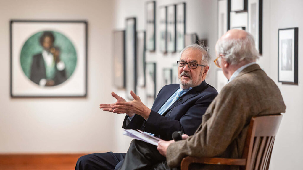 Barney Frank discussing art in gallery surrounded by framed paintings wallpaper background