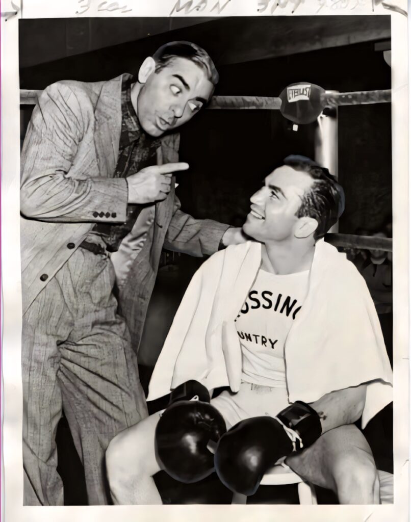 Barney Ross smiling in boxing ring with gloves and towel listening to man in suit wallpaper background
