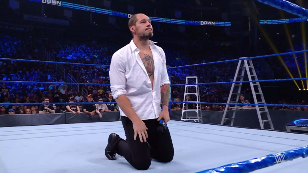 Baron Corbin kneeling in WWE SmackDown ring wearing white shirt and black pants under lights Wallpaper