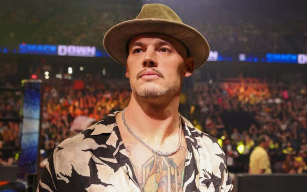 Baron Corbin confident in stylish hat and patterned shirt with vibrant WWE crowd backdrop wallpaper