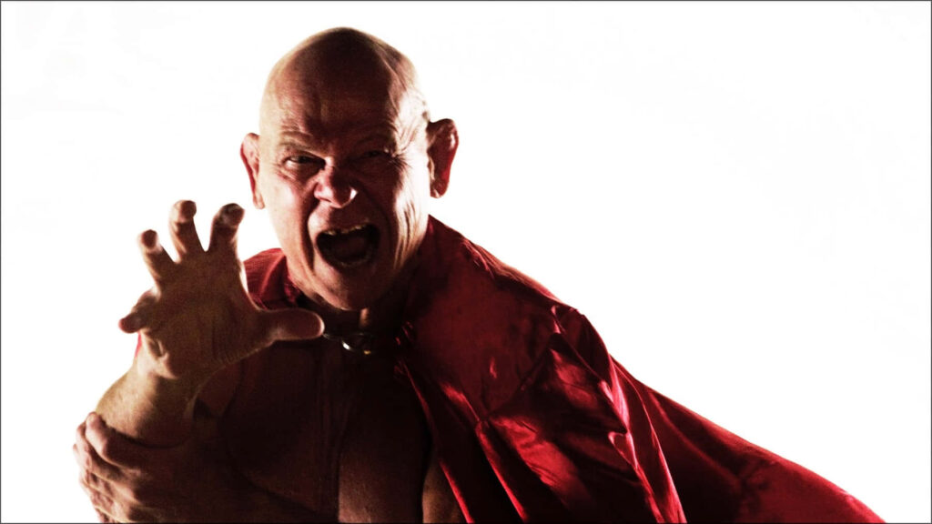 Wrestler Baron Von Raschke in iconic red cape striking fierce pose from documentary show Wallpaper