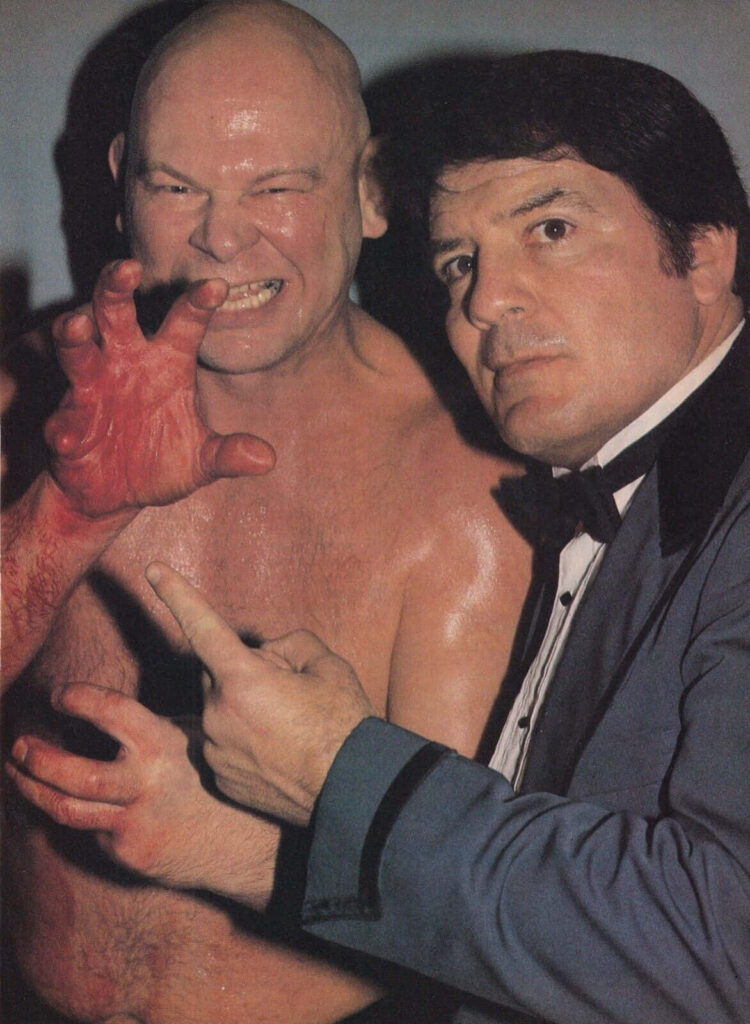 Wrestler Baron Von Raschke striking his iconic claw pose with a well-dressed colleague wallpaper