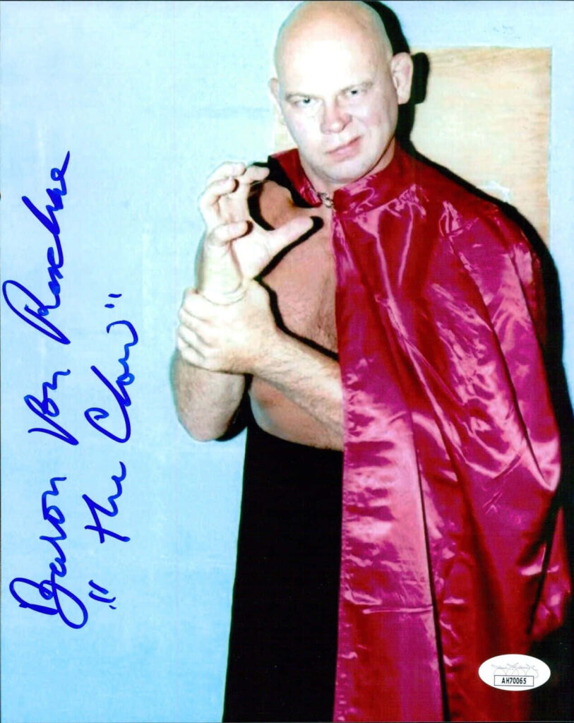 Baron Von Raschke performing The Claw wrestling move in red cape against wallpaper background