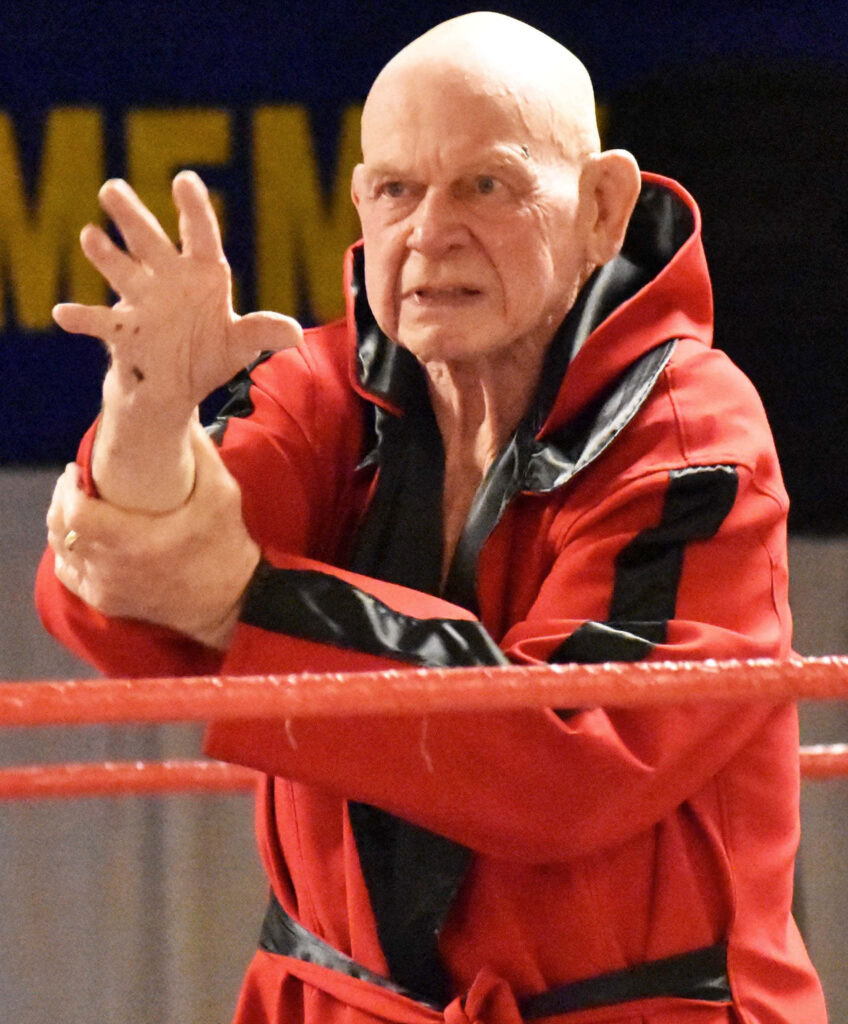 Legendary wrestler Baron Von Raschke in red robe striking signature pose in wrestling ring wallpaper