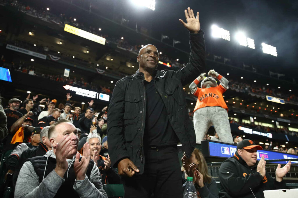 Barry Bonds waving at Giants game with cheering fans and mascot in vibrant stadium background Wallpaper