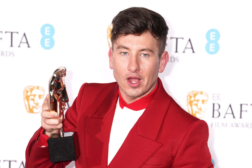 Barry Keoghan in red suit holding BAFTA Award with BAFTA logo wallpaper background