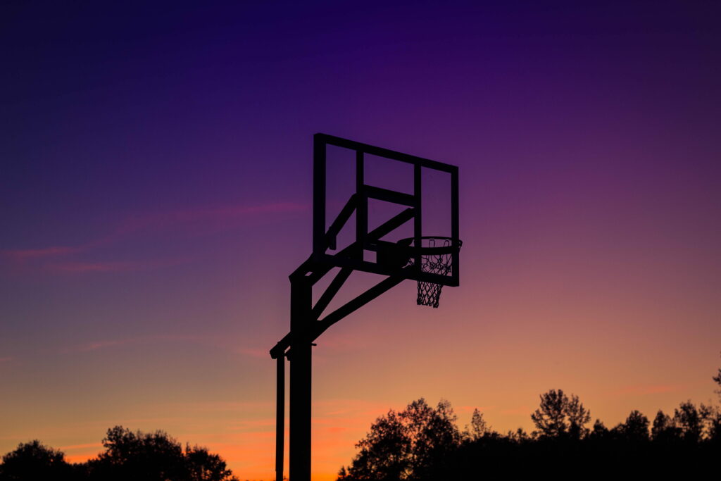 Basketball hoop silhouette at sunset with vibrant sky and dark tree line nature wallpaper