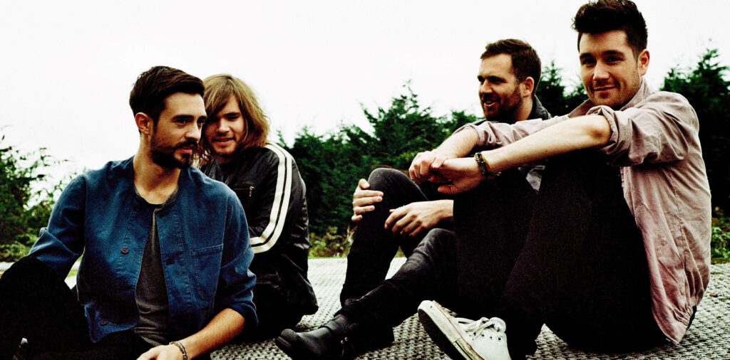 Bastille band members sitting on rooftop with green trees background relaxed moment wallpaper