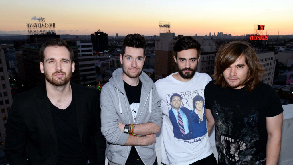 Bastille band members on rooftop with city skyline at sunset music wallpaper background