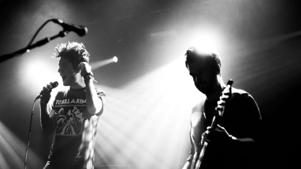 Bastille live concert energetic performance with microphones guitars and dramatic stage lighting Wallpaper