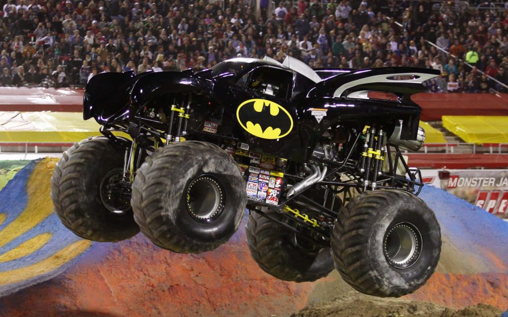 Batman Monster Jam truck launching off ramp in packed arena with iconic yellow bat logo Wallpaper