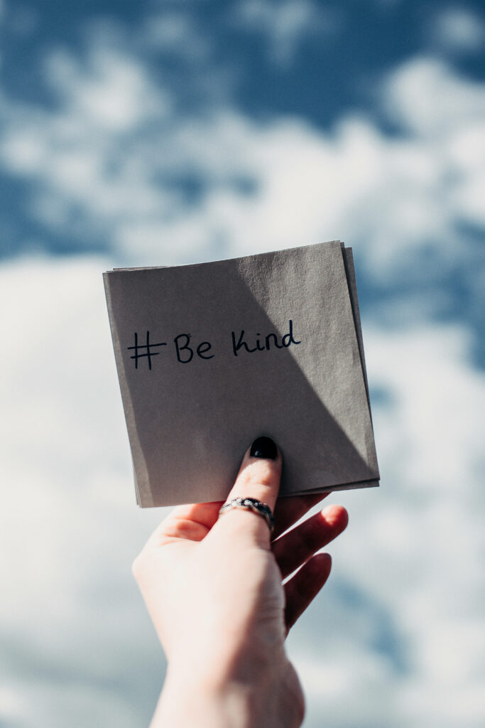 Hand holding Be Kind note against blue sky promoting mental health awareness and kindness Wallpaper
