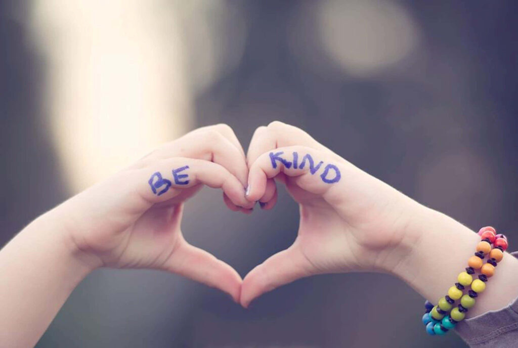 Two hands form heart shape with Be Kind message on fingers soft blurred background wallpaper