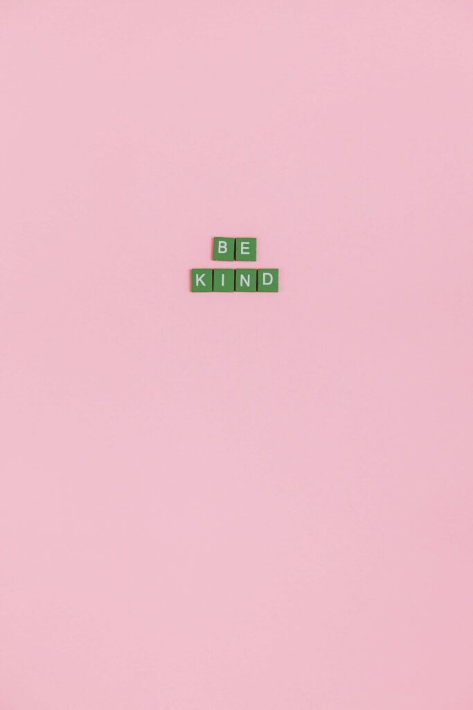 Green letter tiles spelling Be Kind on soft pink background minimal kindness wallpaper design