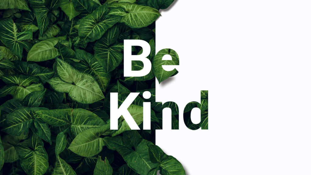 Be Kind bold text wallpaper with lush green leaves background promoting kindness and positivity