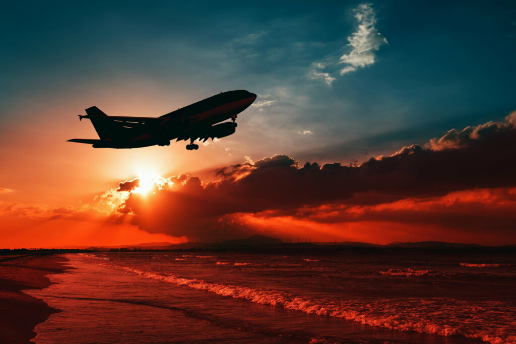 Golden Skies: Majestic Plane Soaring Above Tranquil Sunset Beach Wallpaper