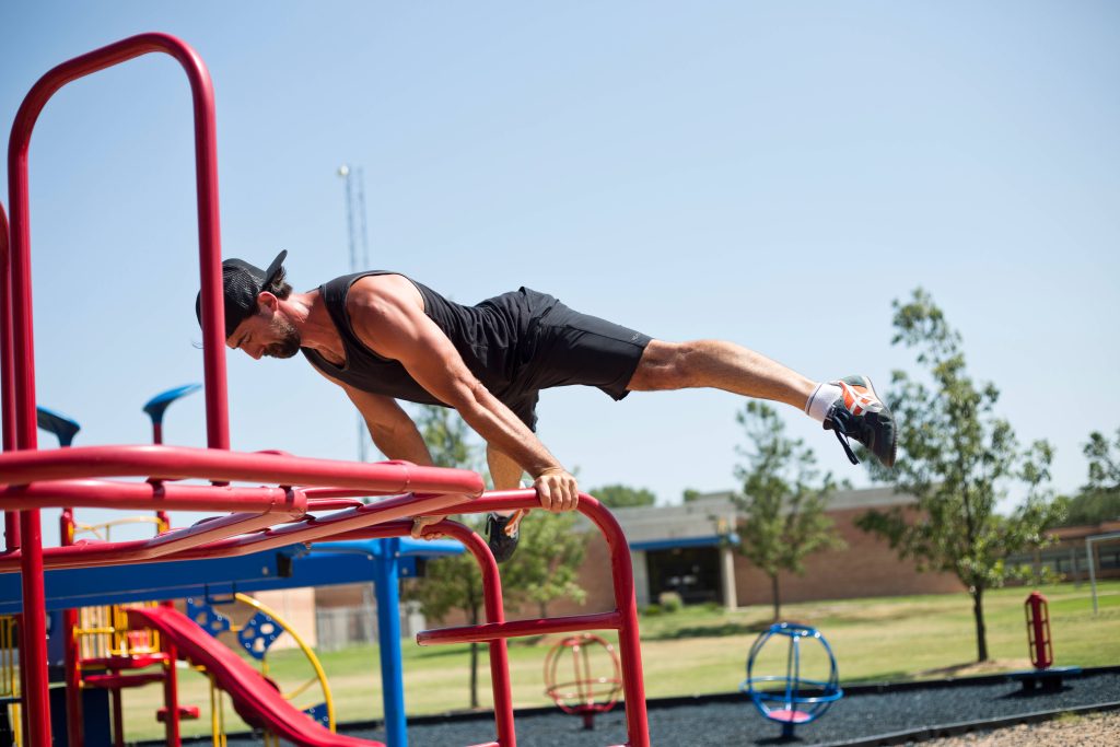 Bearded man performing perfect planche on red bars showcasing core strength in sunny park Wallpaper