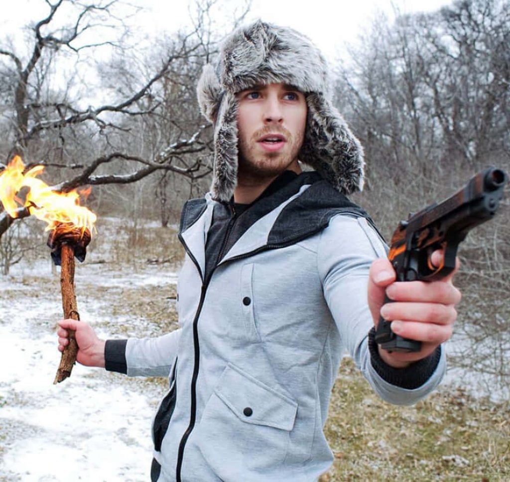 Bearded man in fur trapper hat and hoodie aims handgun with torch in snowy forest winter Wallpaper