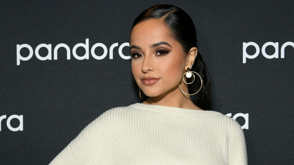 Becky G in large hoop earrings and white top posing confidently at Pandora event backdrop Wallpaper