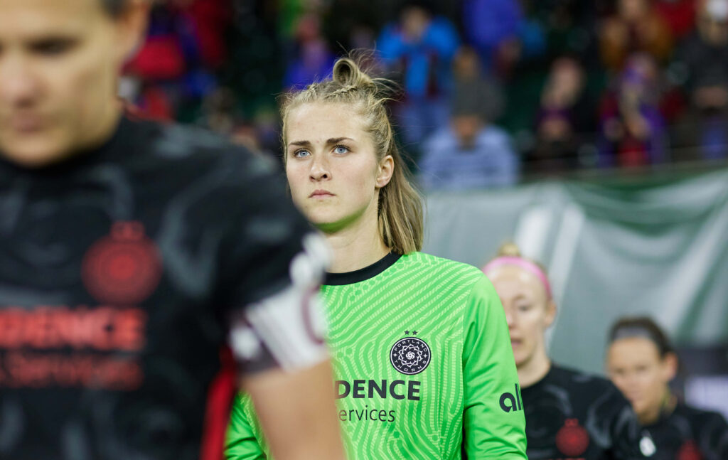 Bella Bixby in green goalkeeper jersey focused during match with teammates in background wallpaper