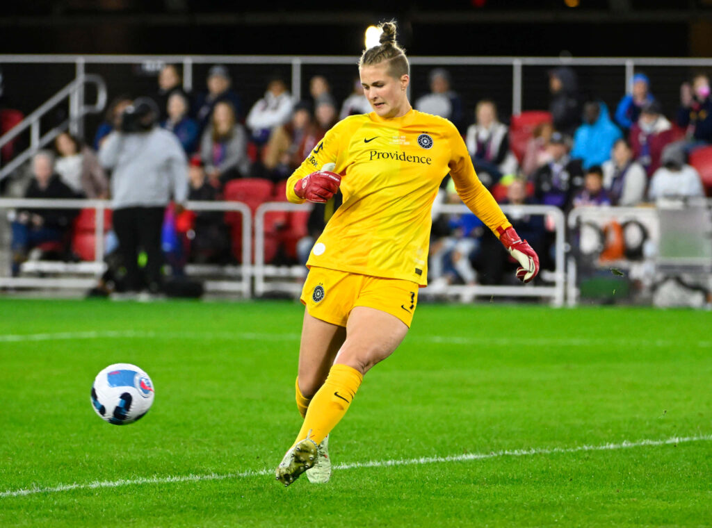 Bella Bixby in yellow goalkeeper kit about to kick ball during intense soccer match action wallpaper