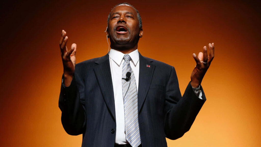 Ben Carson speaking passionately with expressive gestures against warm orange background wallpaper