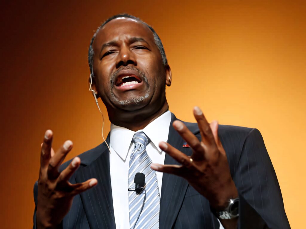 Ben Carson speaking passionately in suit with expressive gestures against golden background wallpaper