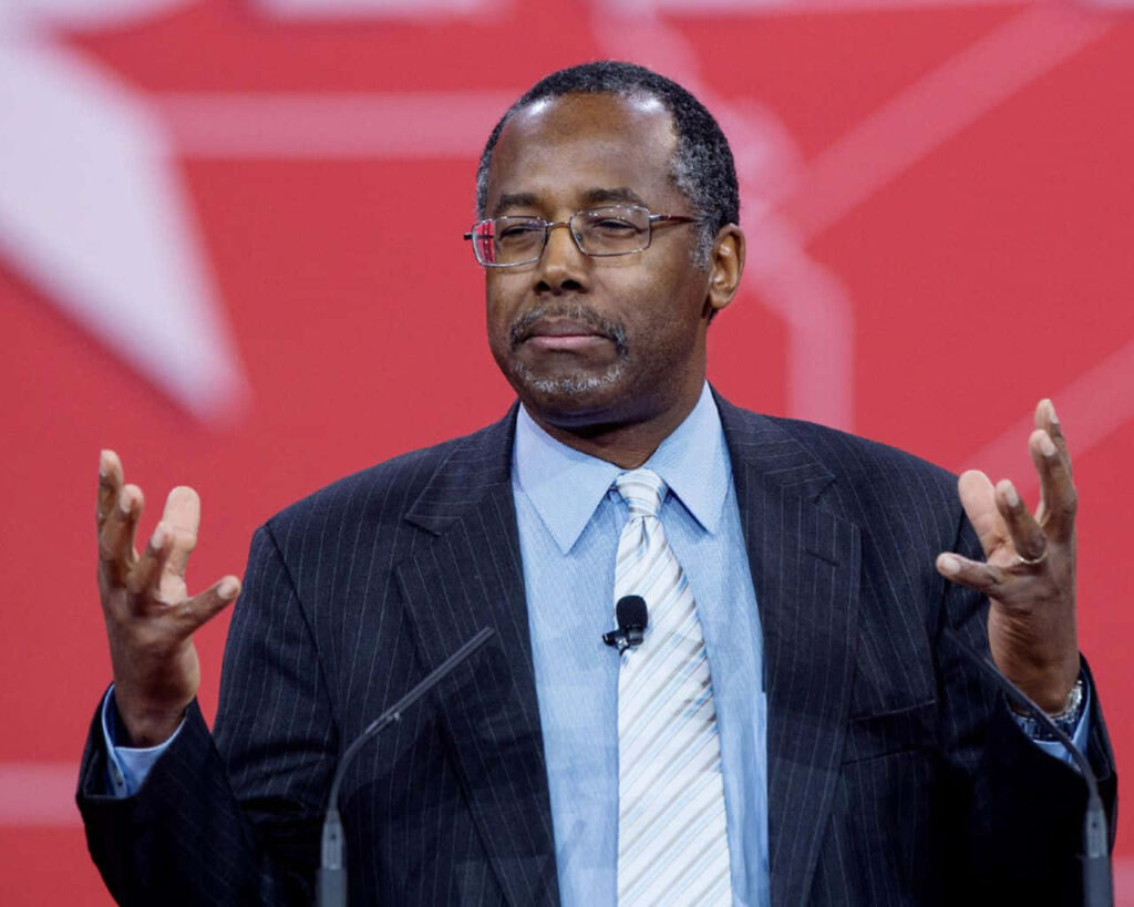 Ben Carson speaking passionately on stage with expressive gesture red background wallpaper
