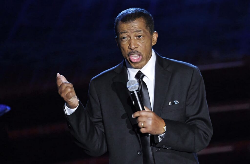 Ben E King singing on stage in black suit holding microphone dramatic lighting wallpaper background