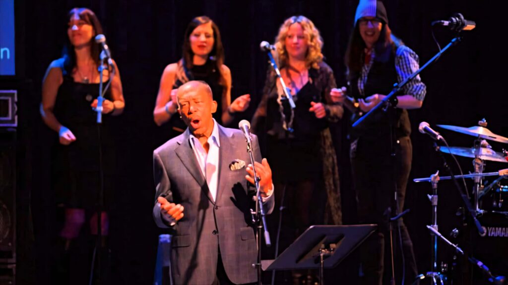 Ben E King singing live with backing vocalists and musicians vibrant concert wallpaper background