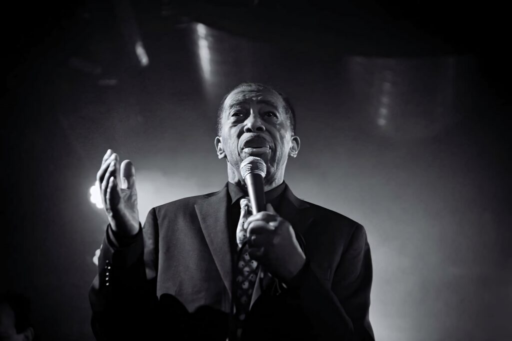 Ben E King soulful monochrome singing performance wallpaper expressing passion on stage background
