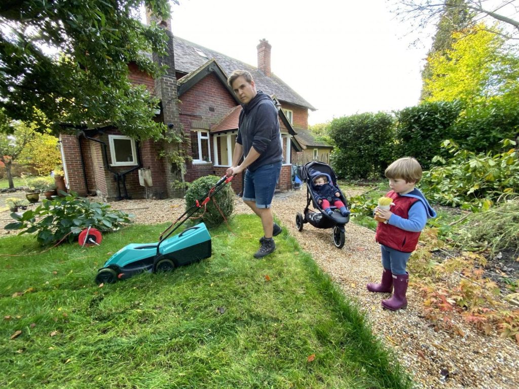 Ben Fogle mowing lawn with turquoise mower babysitting son and baby by brick house front yard Wallpaper
