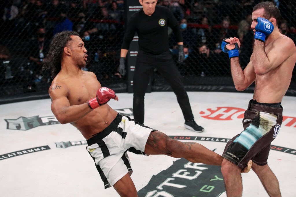 Ben Henderson executing a high inside kick against Islam Mamedov in intense MMA fight cage Wallpaper