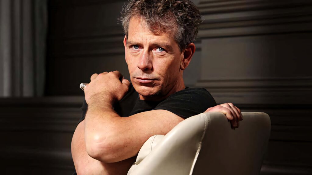Ben Mendelsohn portrait wallpaper seated light chair intense gaze rugged style background