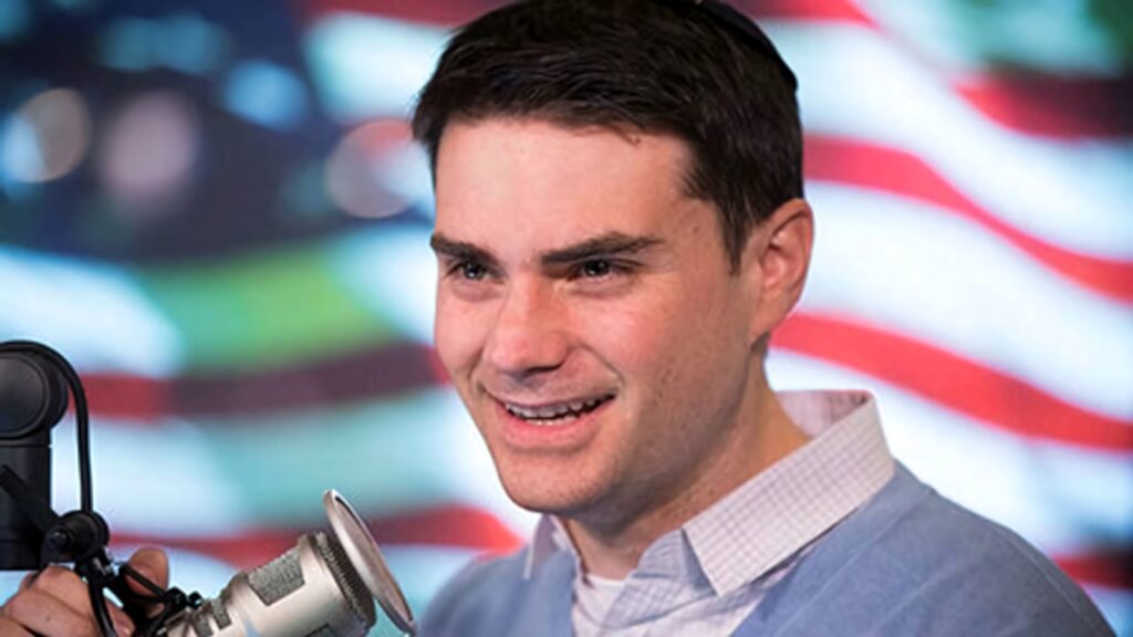 Ben Shapiro American political commentator speaking into microphone with blurred US flag background Wallpaper