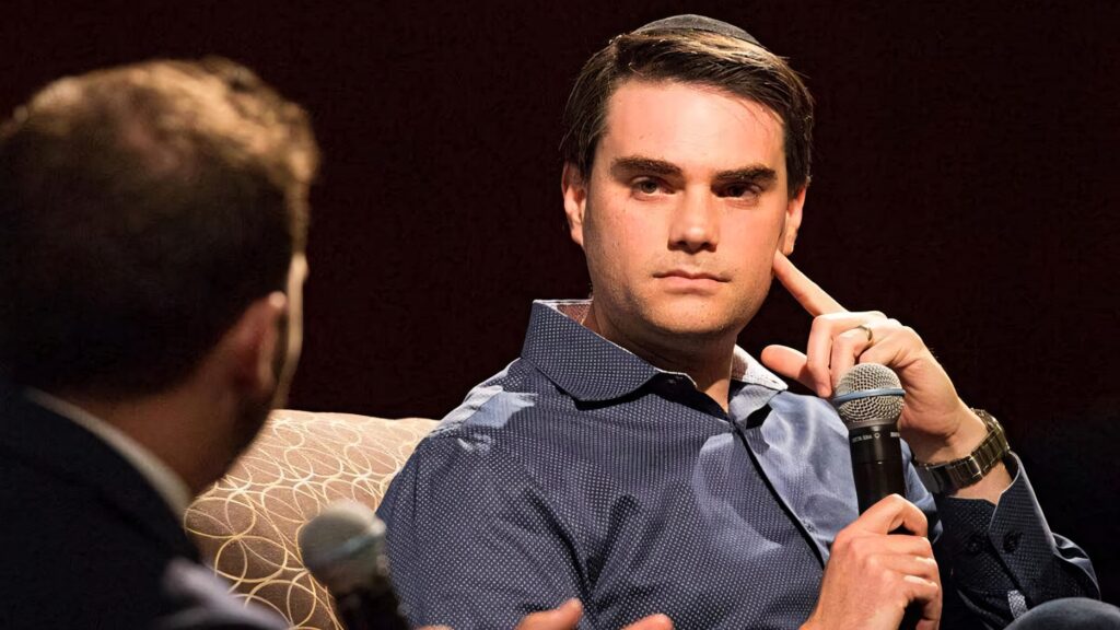 Ben Shapiro attentively listening during interview holding microphone dark wallpaper background