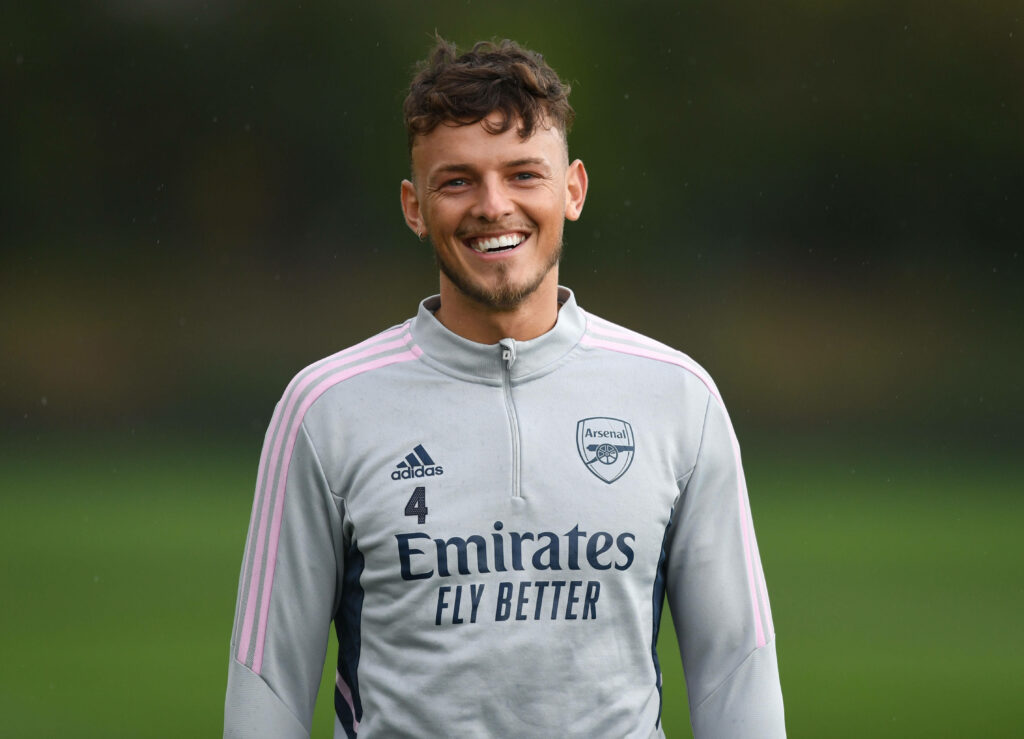 Ben White smiling in Arsenal training kit on green field during positive football practice session Wallpaper