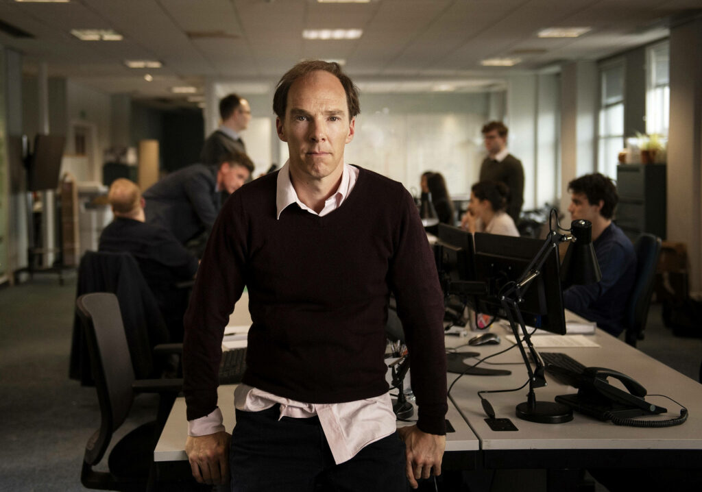 Benedict Cumberbatch confident office worker standing in modern open-plan workspace professional Wallpaper