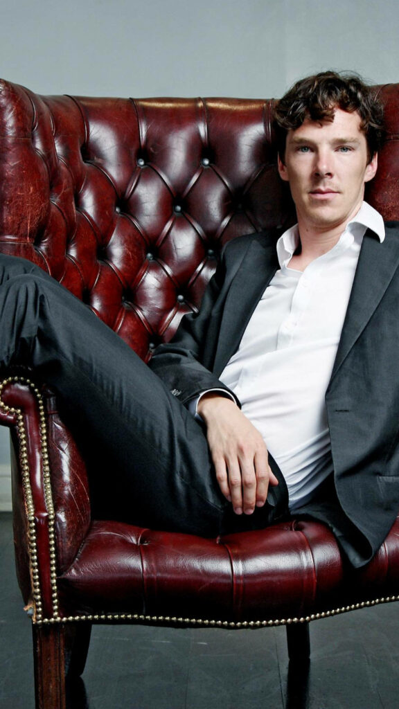 Benedict Cumberbatch in sharp suit seated on classic leather chair with thoughtful confident pose Wallpaper