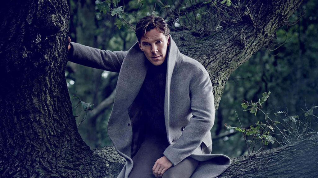 Benedict Cumberbatch in grey coat sitting on tree branch in forest thoughtful gaze wallpaper background