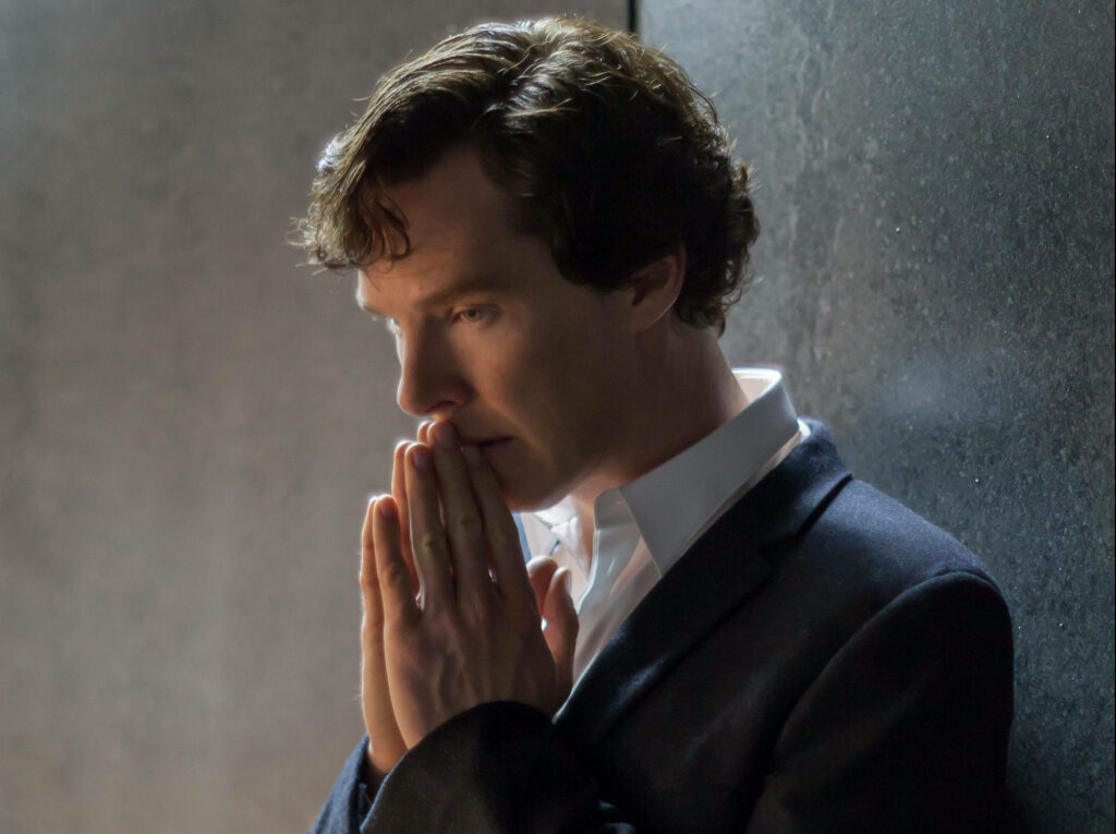 Benedict Cumberbatch in contemplative pose with hands pressed praying against dark backdrop Wallpaper