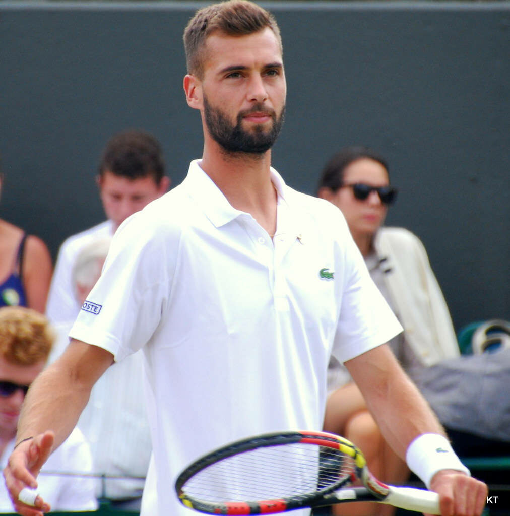 Benoît Paire in white tennis shirt on court poised for match with wallpaper background