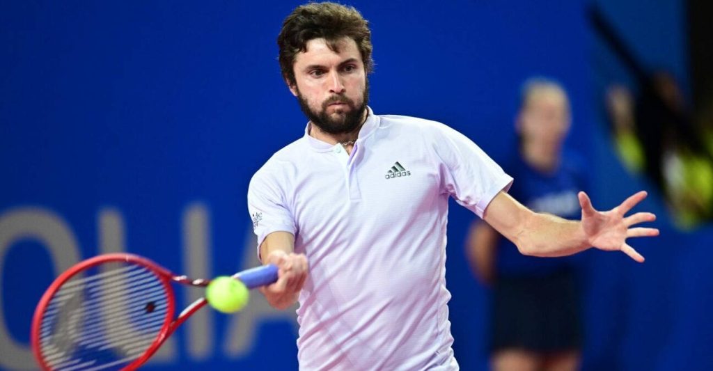 Professional tennis player Benoît Paire hitting a focused forehand on vibrant blue court in Adidas polo Wallpaper