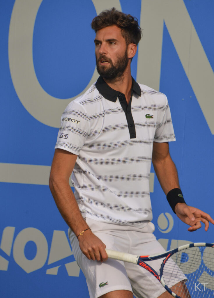 Benoît Paire tennis player in Lacoste gear focused preparing next move on vibrant blue court background Wallpaper