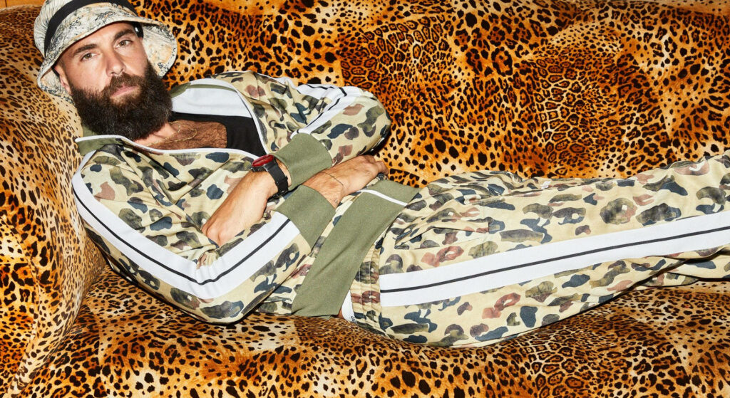 Benoît Paire in bold leopard print tracksuit and hat lounging on matching leopard print sofa background Wallpaper