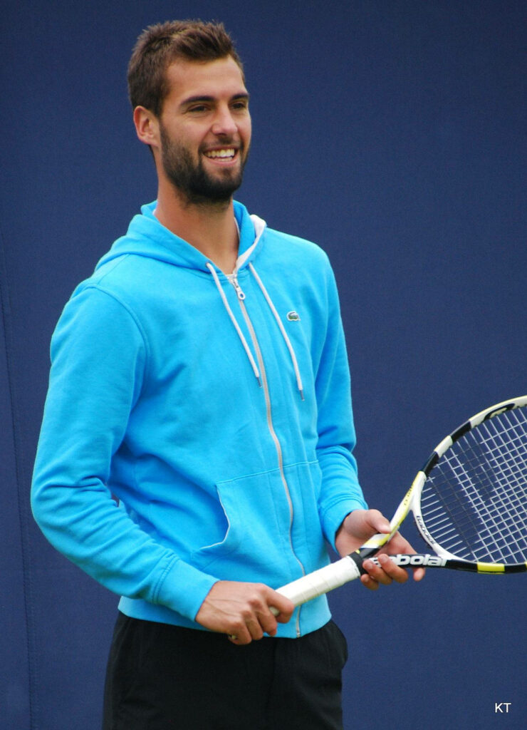 Benoît Paire smiling in bright blue hoodie holding tennis racket against solid blue background Wallpaper