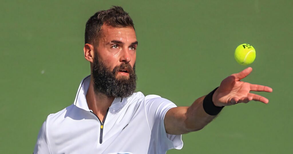 Tennis pro Benoît Paire focused serving during match on court with blurred wallpaper background