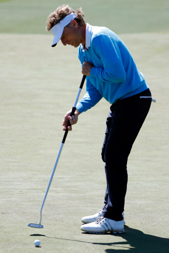 Bernhard Langer in blue sweater and visor concentrating on putting golf ball on course wallpaper