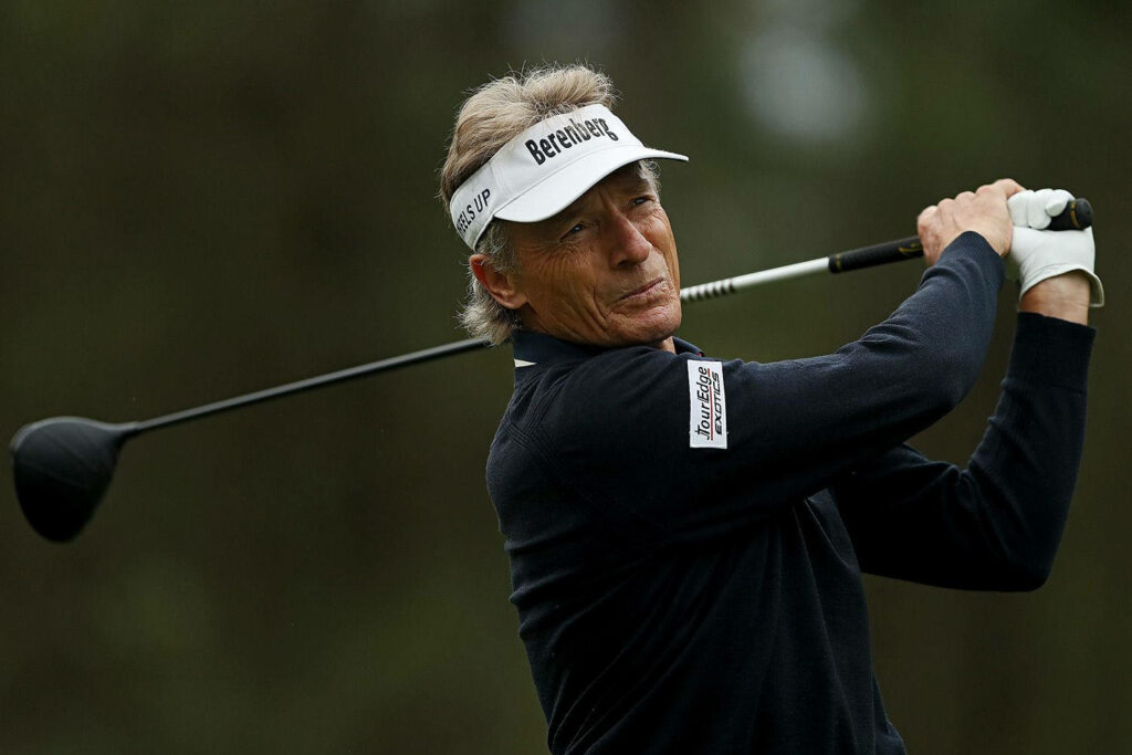 Bernhard Langer focused golf swing in white cap on course with wallpaper background