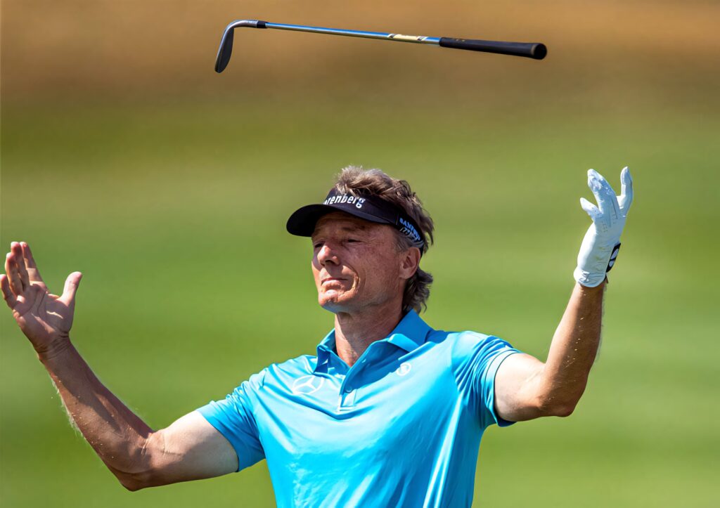 Bernhard Langer tossing golf club on vibrant green golf course showing skill and focus play Wallpaper